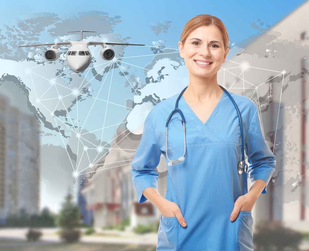 A smiling nurse in blue scrubs with a stethoscope around her neck, standing with her hands in her pockets. Blog title: Can a Registered Nurse Be a Travel Nurse?