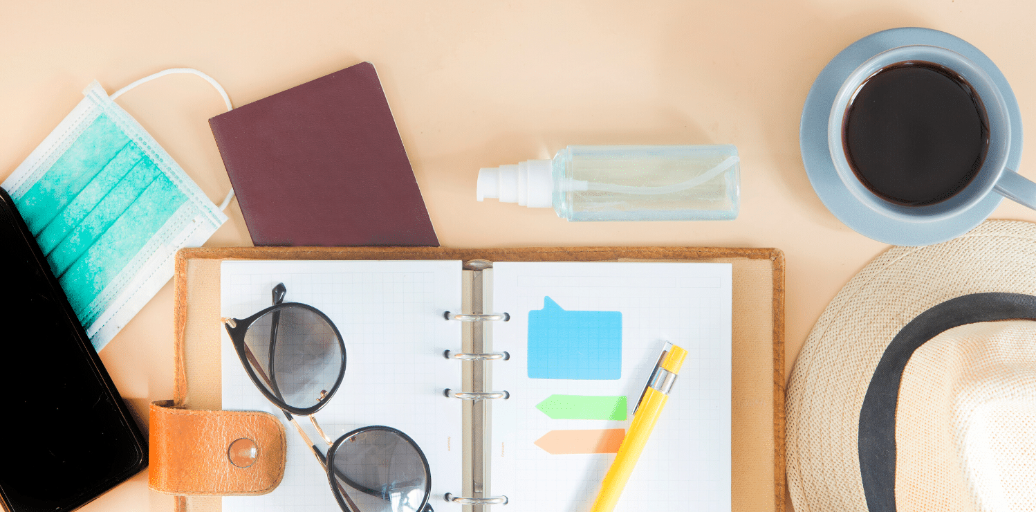 Desk with various items placed on it including a face mask, hand moisturizer, coffee mug, hat, sunglasses, planner, pen, and cellphone. This image suggests the person is a travel nurse preparing for the holiday season.