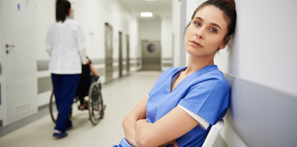 Image of a female nurse sitting with her arms crossed and a stressed expression on her face. Nursing in Crisis Urgent Crossroads for the Future of U.S. Healthcare Ecosystem