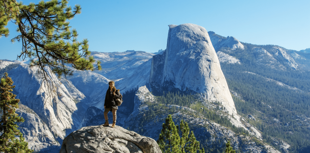 An adventurous woman in camping gear, exuding excitement, explores the breathtaking Yosemite National Park on the West Coast of the United States. Towering mountains, lush greenery, and a sense of wonder surround her as she embraces the beauty of nature.