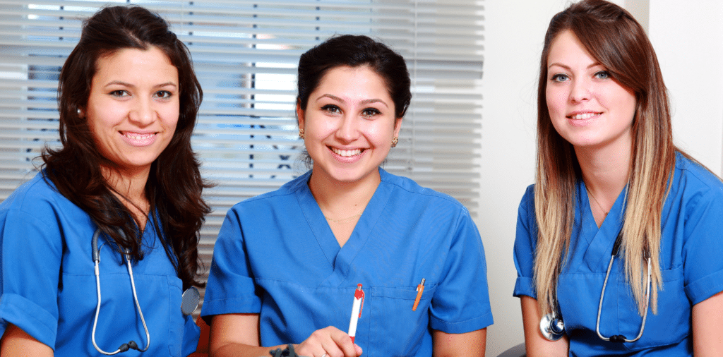 Three enthusiastic new nurses dressed in blue scrubs, ready to begin their exciting travel nursing journey.