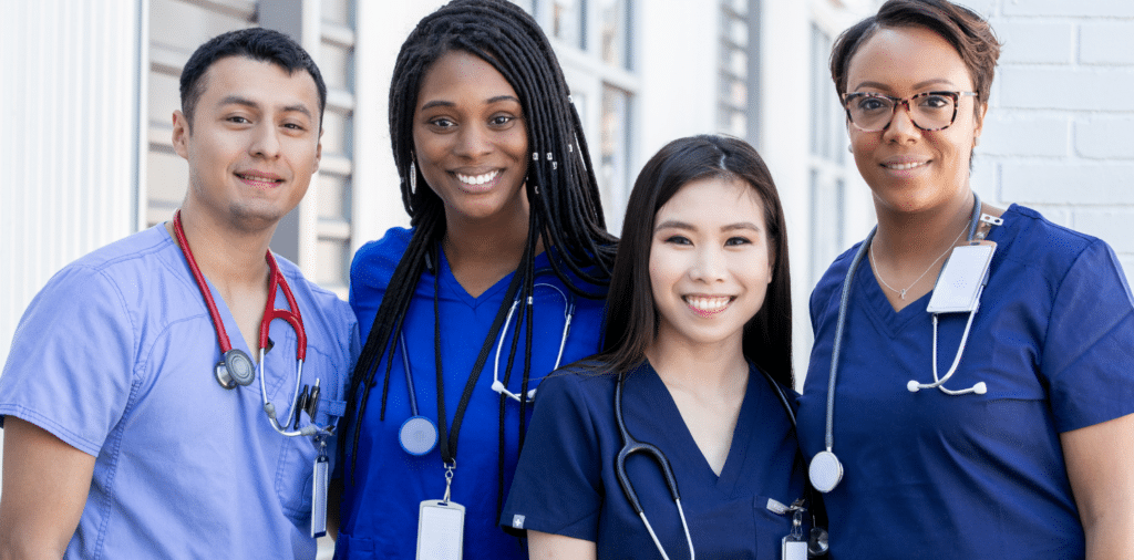 Four travel nurses posing confidently in blue scrubs and stethoscopes. The group is smiling and radiating positive energy as they showcase their passion for healthcare.