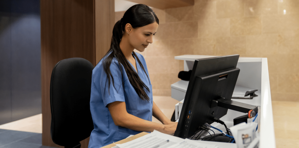 A travel nurse sitting at a computer, conducting research to find the best travel nurse recruiters and agencies