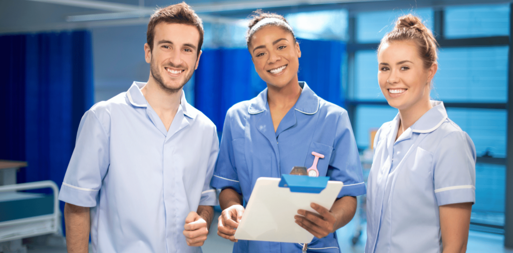 Three nurses representing diverse nursing specialties stand side by side in a hospital room, wearing blue scrubs and beaming with smiles. Two of the nurses are female, while the other is male. Their shared enthusiasm and camaraderie shine through as they showcase the unity and teamwork within the nursing profession.
