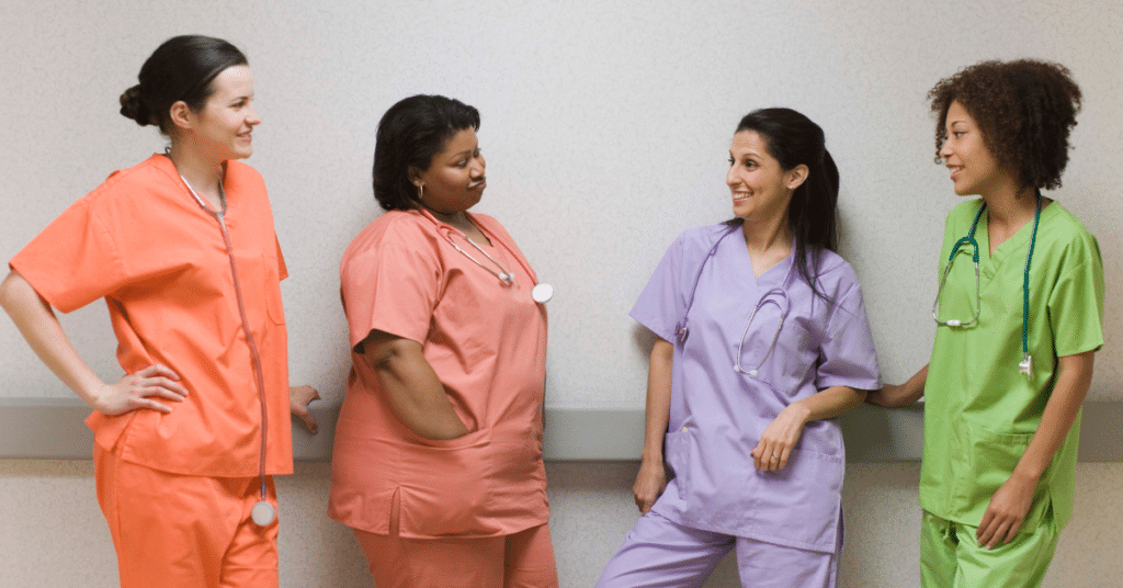 A group of diverse nurses in a hospital setting, standing together wearing vibrant and colorful scrubs. The nurses represent the comparison between travel nursing and staff nursing, showcasing the unique benefits and experiences each role offers. Travel nursing offers a dynamic journey through various healthcare environments and locations, while staff nursing provides stability within a specific healthcare institution. The image captures the essence of choice, diversity, and camaraderie in the nursing profession. Travel Nursing vs Staff Nursing