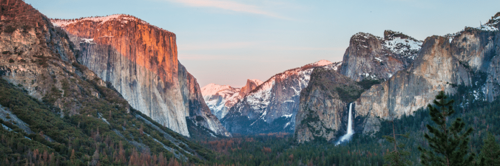 A breathtaking view of Yosemite National Park's iconic landscape, featuring towering granite cliffs, cascading waterfalls, and ancient sequoia trees. This image captures the awe-inspiring beauty of one of California's most treasured national parks.
