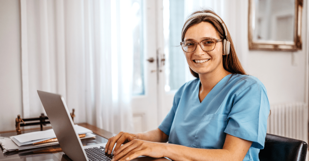A smiling nurse engrossed in her laptop screen at a medical clinic, wearing headphones as she listens to podcasts for nurses, staying updated and entertained while working.