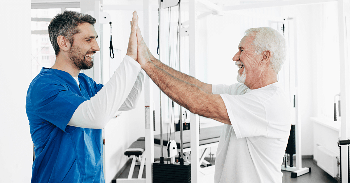 A senior man and a physical therapist joyously high-five each other after a successful physio rehabilitation treatment. This heartwarming scene exemplifies the vital role of physical therapists in helping individuals of all ages to recover, restore mobility, and improve their overall quality of life.