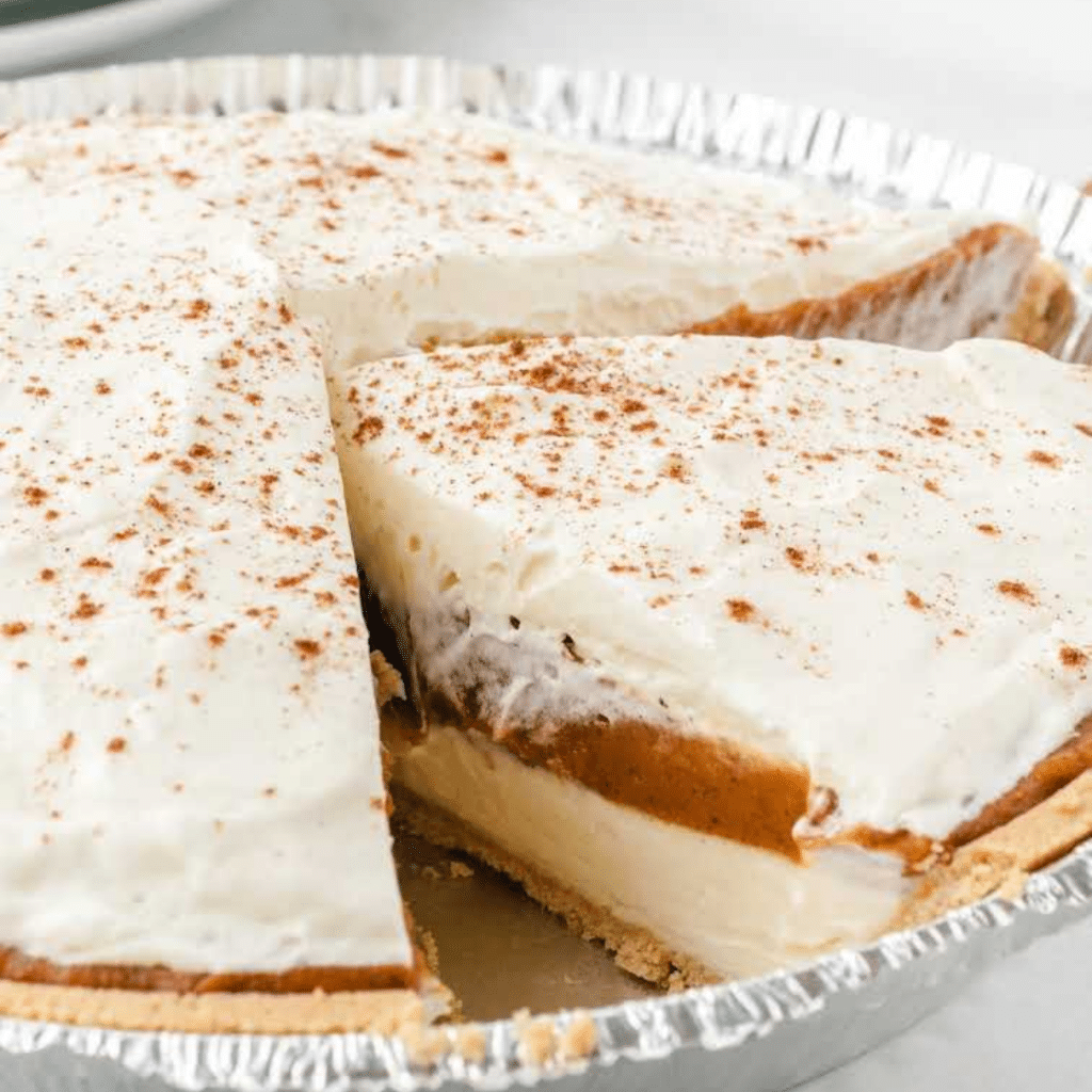 A delicious No-Bake Pumpkin Pie, beautifully garnished with whipped cream and a sprinkle of cinnamon, served on a festive Thanksgiving table setting. This easy-to-make dessert is a perfect choice for travel nurses and allied health professionals looking to create a cozy atmosphere in their temporary home during the Thanksgiving season.