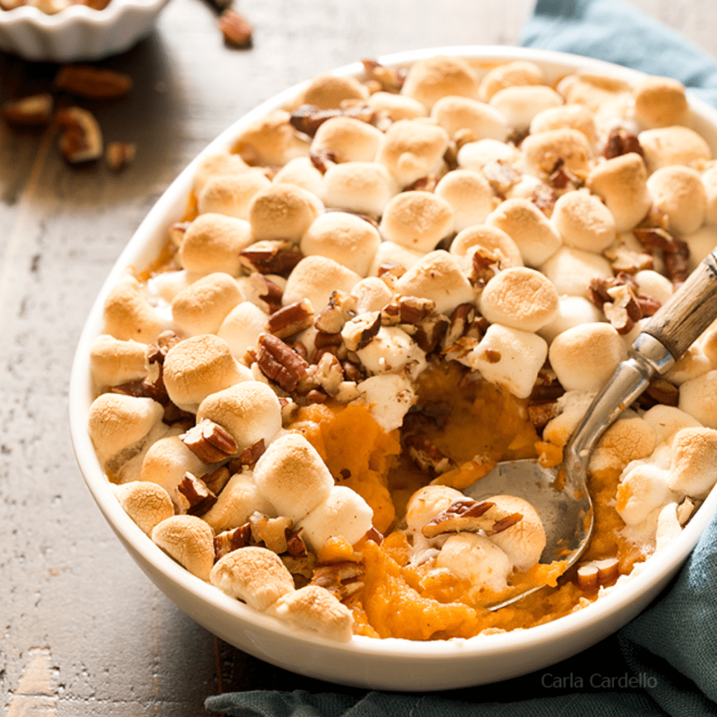 A mouthwatering Sweet Potato Casserole, beautifully prepared and served in a festive dish. This dish is a perfect meal for travel nurses working on a temporary assignment during Thanksgiving to make their home feel cozier and more festive. The casserole is topped with a golden-brown marshmallow and pecan topping, adding a delicious touch to the holiday spirit.