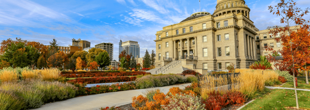 The image depicts the downtown skyline of Boise, Idaho, with the Idaho State Capitol building as a prominent feature. It is set in the fall season, showcasing the beauty and tranquility of the city, making it an appealing yet underrated destination for travel nurses seeking new experiences.