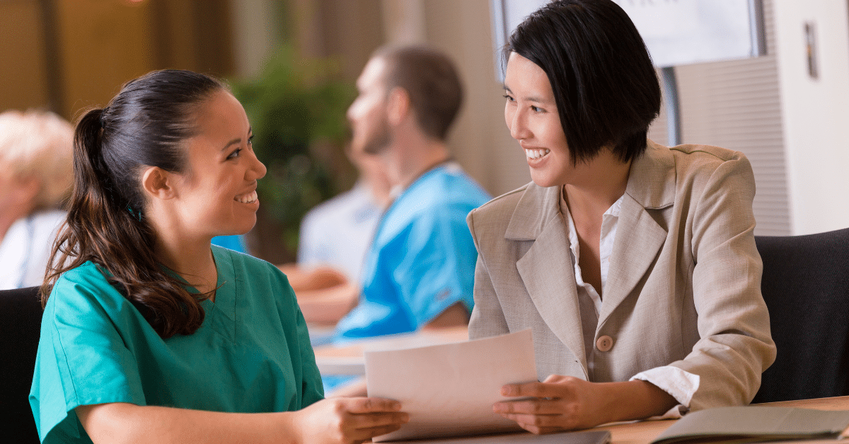 A cheerful travel nurse sits across the table, confidently presenting her resume to a new recruiter as she makes the decision to switch recruiters mid-assignment. She exudes positivity and professionalism, with a bright smile indicating her readiness for new opportunities.