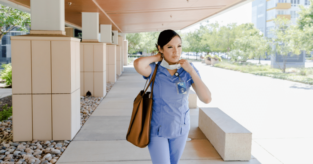 A travel nurse removes her face mask, revealing a slight smile, as she steps outside the healthcare facility, signifying the end of her shift and the transition between her nursing assignments. Her eyes reflect a sense of accomplishment and readiness for the next adventure in her career.